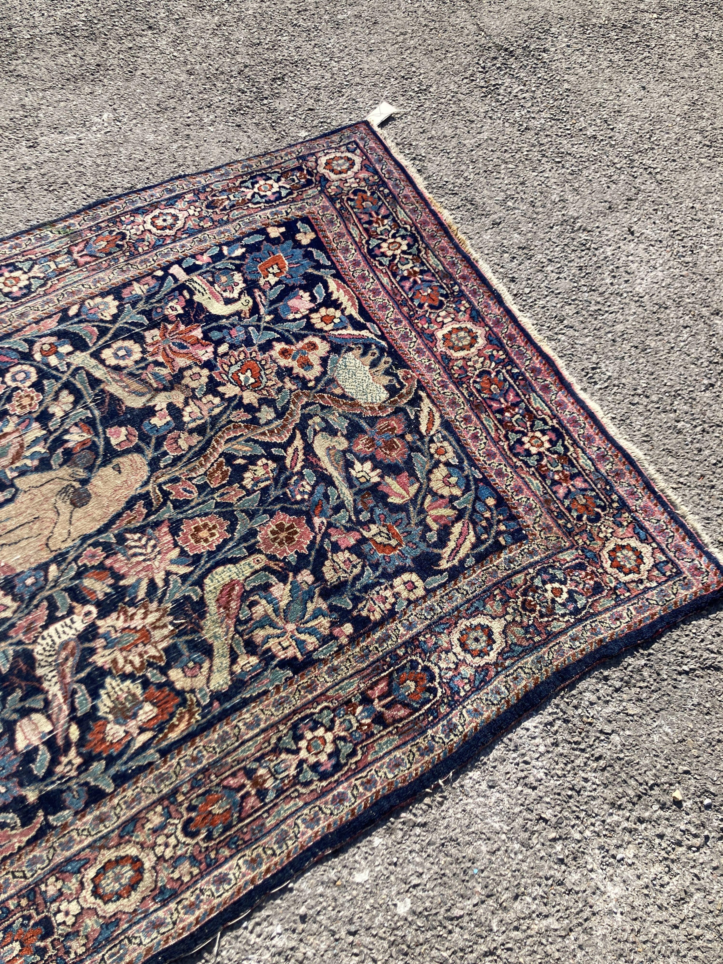 A Persian rug with a central Tree of Life interspersed with animals to include a seated monkey within the tree, a recumbent lion at the base, set within floral borders, 201 x 120cm